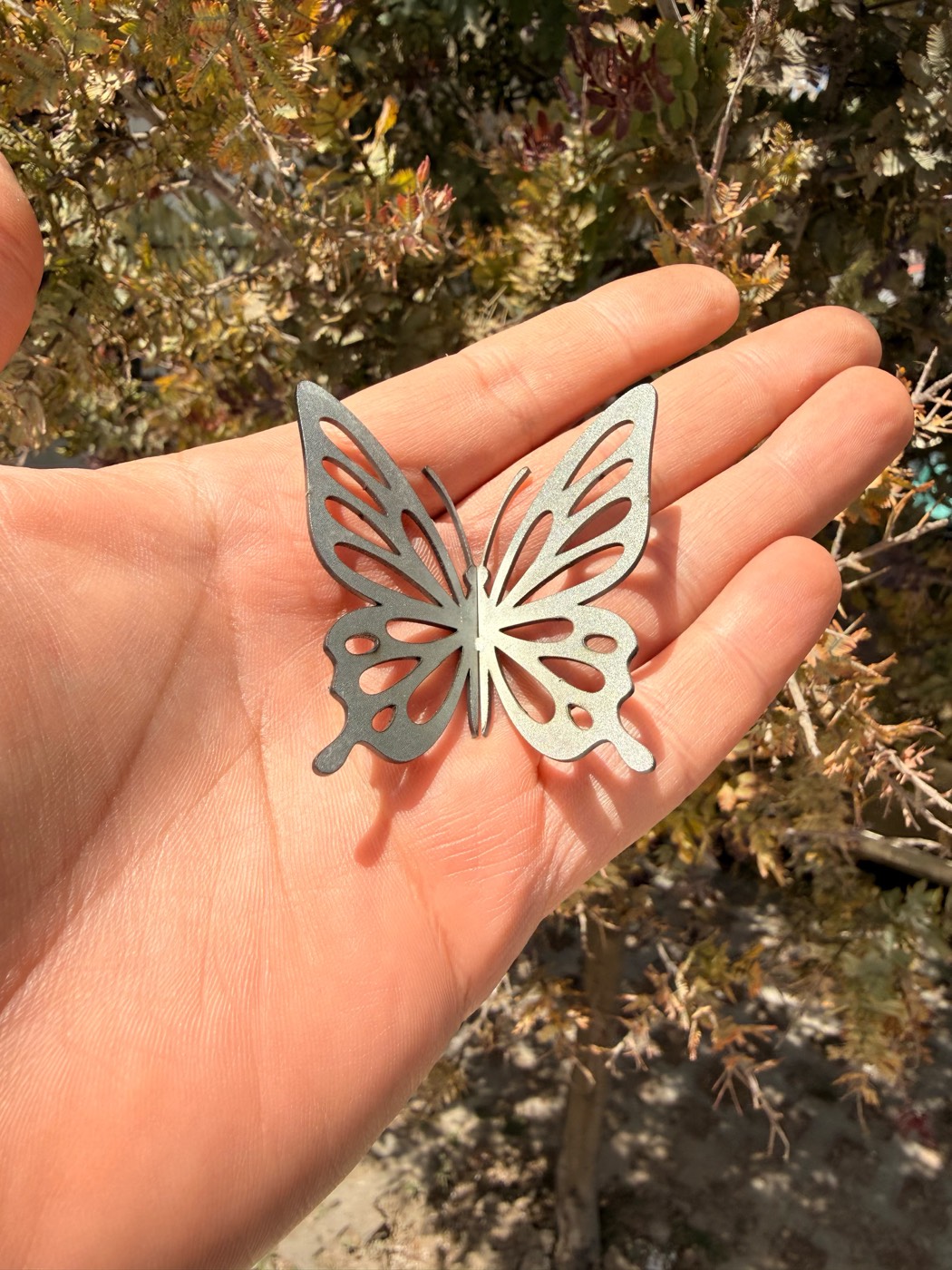 Mariposa calada en acero, cortada con láser en Pachuca, sobre la palma de una mano